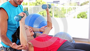 Fit woman lifting dumbbells on blue exercise ball with trainer