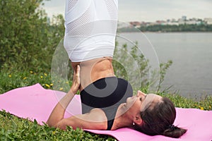 Fit woman making yoga in shoulderstand pose exercising in nature