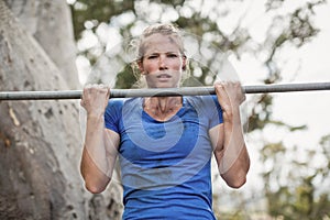 Fit woman performing pull-ups on bar during obstacle course