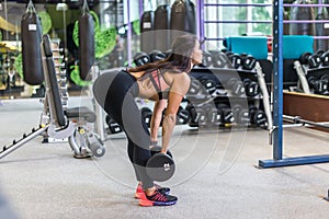 Fit woman performing weight lifting deadlift exercise with dumbbell at gym