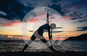 Fit woman practicing the extended triangle yoga pose on a dreamy beach