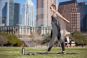 Fit woman practicing yoga and stretching outdoors in urban city setting on grassy lawn, muscular legs and toned butt