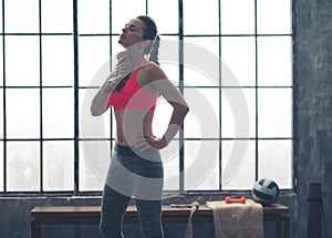 Fit woman in profile wiping sweat off neck in loft gym