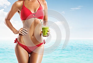 Fit woman in a red bikini holding a green smoothie on the beach