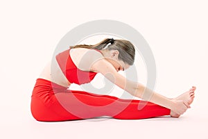 Fit woman in red sportswear stretching her legs to warm up - isolated over white background