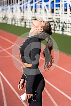 Fit woman resting after workout or running listens to music with wired headphones on smartphone , taking a break during training