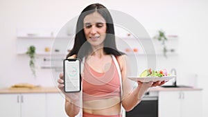 Fit woman showing cellphone screen with calorie counting app