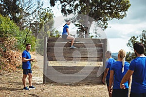 Fit woman sitting over wooden wall during obstacle course