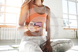 Fit woman sitting on yoga mat and hold mobie phone in hand counts calories in fitness application after training