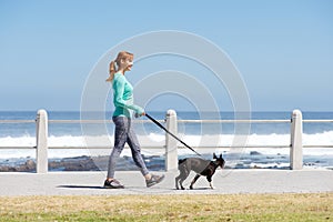 Fit woman smiling and walking dog on path by sea
