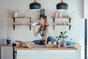 Fit woman in split position on the kitchen table having breakfast.