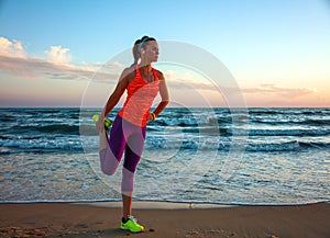 Fit woman in sports gear on beach at sunset stretching