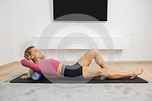 Fit woman in sportswear ride on foam myofascial massage roller, massaging their muscles in yoga mat