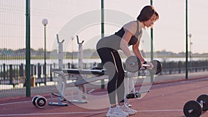 Fit woman strengthens muscles of back lifting heavy barbell