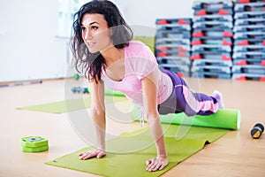 Fit woman stretching on floor using foam roller doing plank exercise, push ups