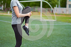 Fit woman stretching her leg to warm up. On football field