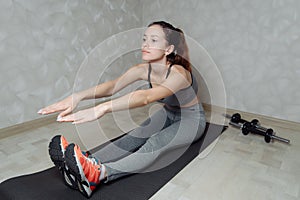 Fit woman stretching her leg to warm up on grey mat at home. Fitness concept, close up on sport shoes