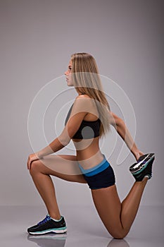 Fit woman stretching her leg to warm up over grey background