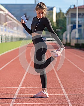 Fit woman stretching muscles making functional training, doing exercises for legs, hamstring stretch before jogging, holding phone