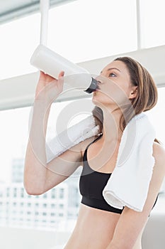 Fit woman with towel around neck drinking water in fitness studio
