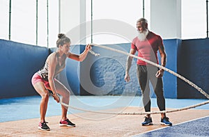 Fit woman training with battle rope inside gym - Personal trainer motivating a female athlete doing workout session exercises