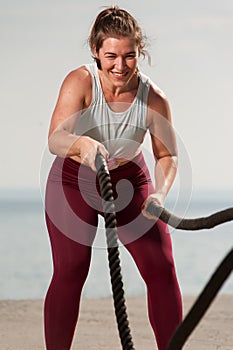 Fit woman training with battle ropes on the beach