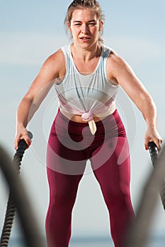 Fit woman training with battle ropes on the beach