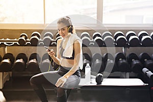 Fit woman using headphone and listening to music while sitting with relax after the training session in gym,Concept healthy and li