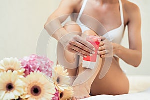 Fit woman waxing her legs with a portable roll-on depilatory wax