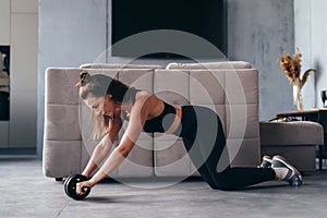 Fit woman working out with ab exercise wheel at home.