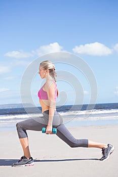 Fit woman working out with dumbbells on the beach lunging