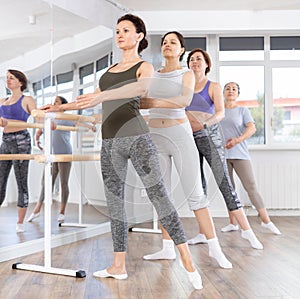 Woman performing battement tendu at ballet barre at beginners group class photo