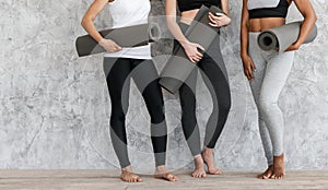 Fit women in sportswear standing with fitness mats in hands near wall