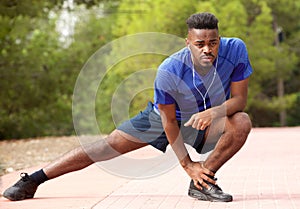 Fit young african american man doing stretching exercise while listening to music with earphones