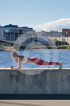 Fit young athletic woman in pink legging doing plank exercise working on abdominal muscles and triceps outdoors