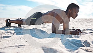 Fit young black man doing plank hold exercises on sand at the beach in the morning. One muscular male bodybuilder