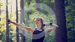 Fit young blonde woman working out with dumbbells outside