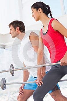 Fit young couple holding barbells in the gym