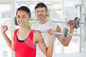 Fit young couple lifting barbells in gym