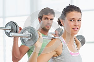 Fit young couple lifting barbells in gym