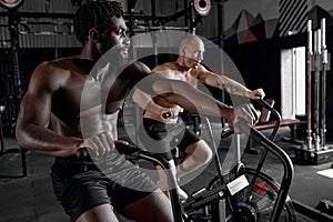 Fit young diverse men using exercise bike at modern gym. Fitness male using bike