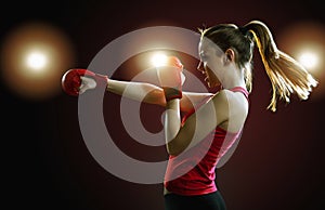 Fit, young, energetic woman boxing, black background