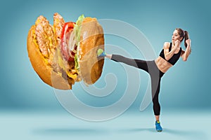 Fit, young, energetic woman boxing hamburger as unhealthy food