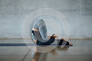 Fit young female trainer practices individual hatha yoga on a mat in a gray background, pilates studio