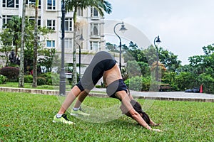 Fit young lady working out outdoors, doing stretching exercises and standing in downward facing dog yoga pose.