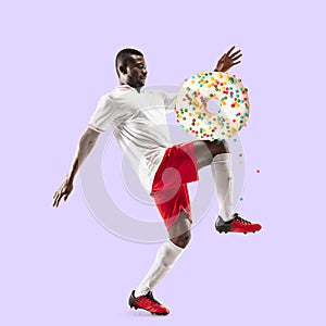 Fit young man fighting off bad food on color background. Male soccer football player with sweet donuts. Healthy eating