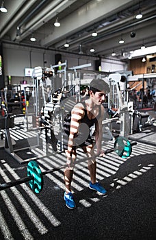 Fit young man in gym working out, lifting barbell.