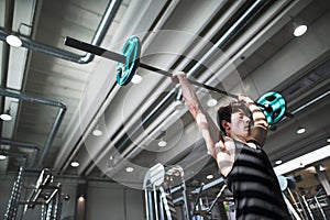 Fit young man in gym working out, lifting barbell. Copy space.