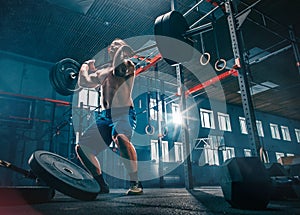 Fit young man lifting barbells working out in a gym
