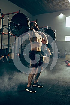 Fit young man lifting barbells working out in a gym